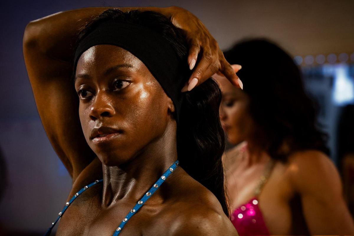Female competitor fixing her hair backstage, another athlete behind her