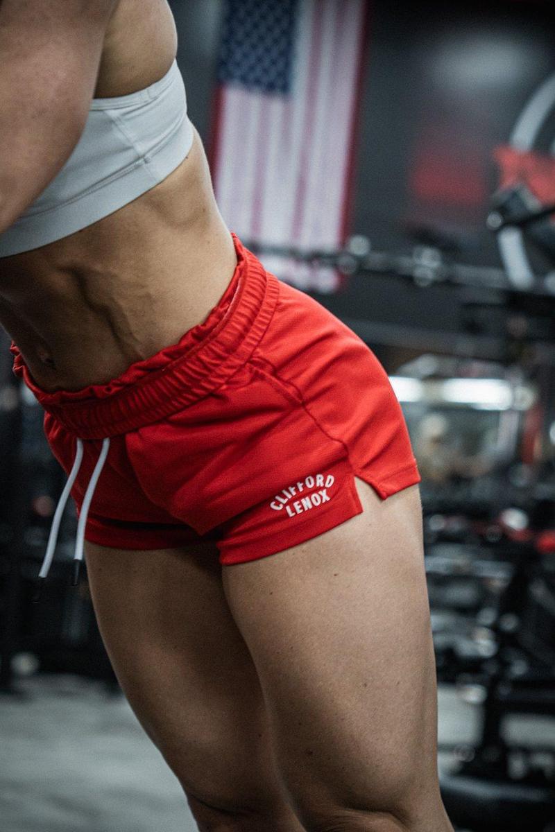 Athlete in red Clifford Lenox shorts leaning into a pose, an American flag behind her