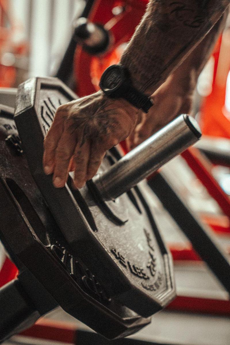 Tattooed hand loading a plate onto a machine in a red gym