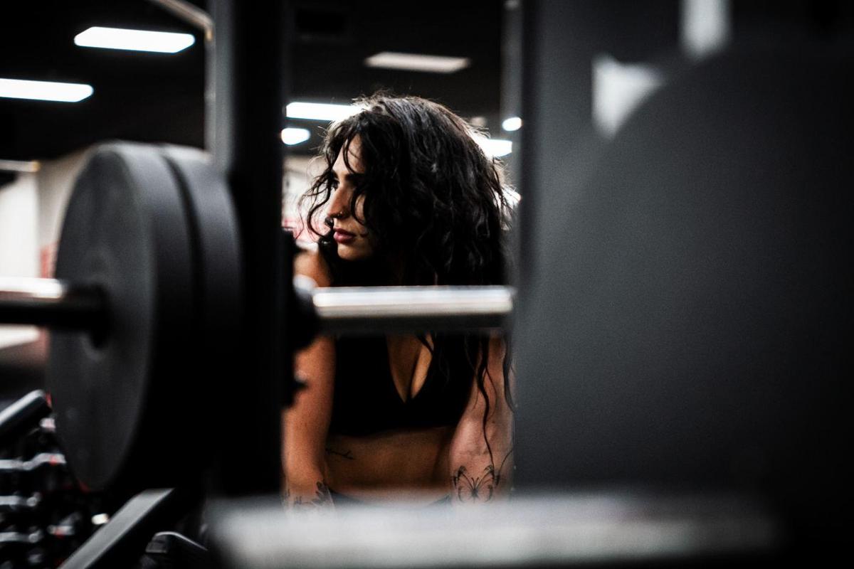 Female athlete framed between barbell plates in a dark gym