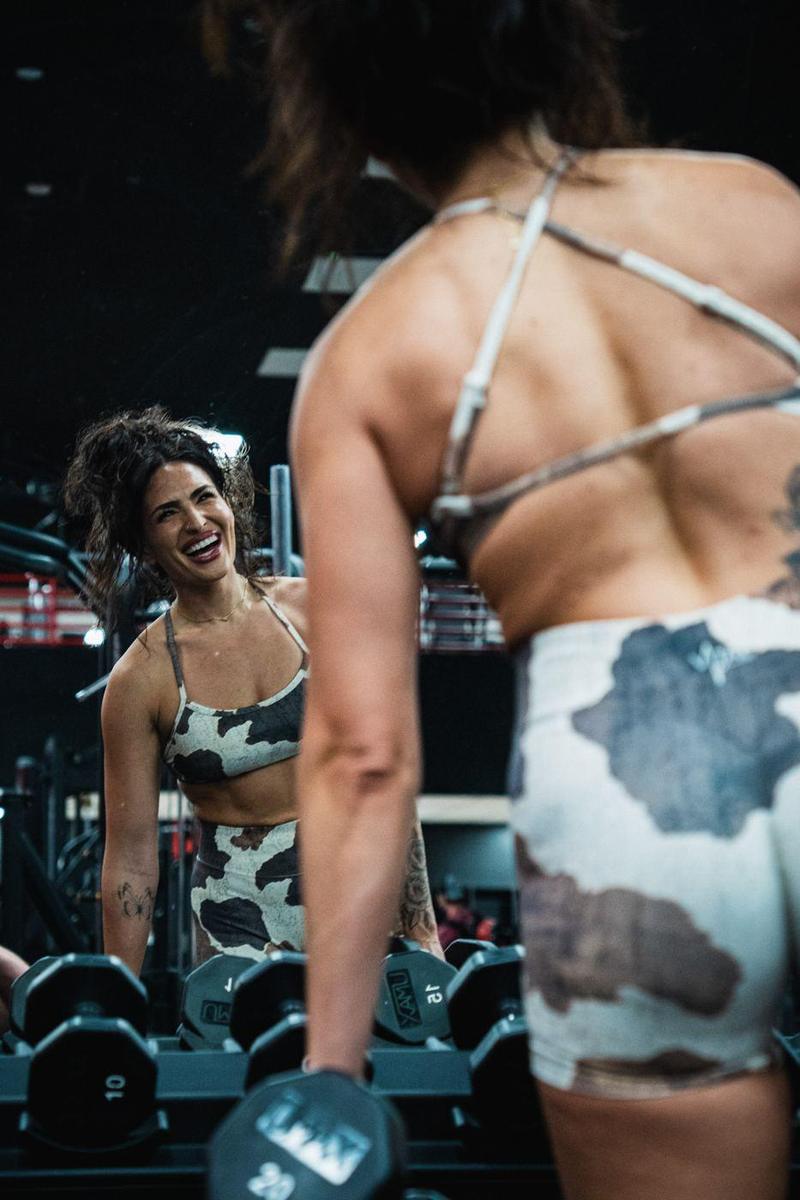 Female athlete laughing at her reflection at the dumbbell rack