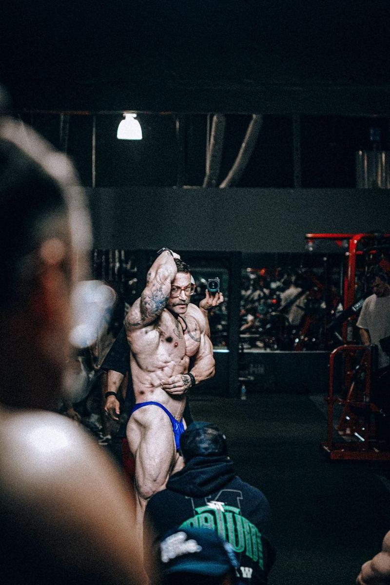 Athlete practicing an abs and thigh pose in a gym while others watch