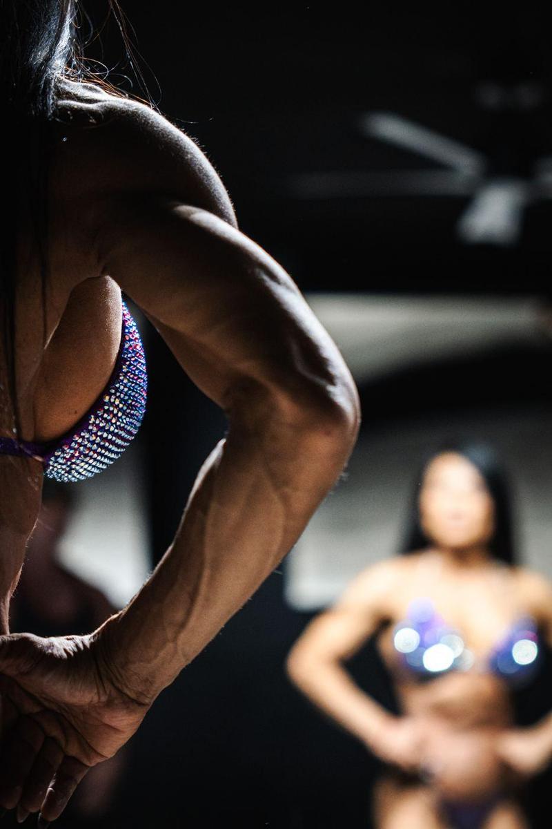 Close detail of a competitor's arm in a rear pose, another competitor blurred behind