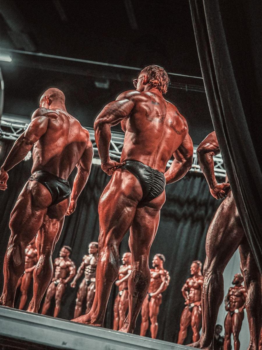 Competitors on stage seen from behind, the lineup reflected across the stage